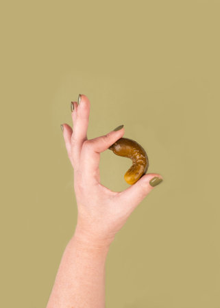A woman's hand holds a pickle and shows an OK gesture. Concept of holiday Shape Up With Pickles Time. vertical shotの写真素材