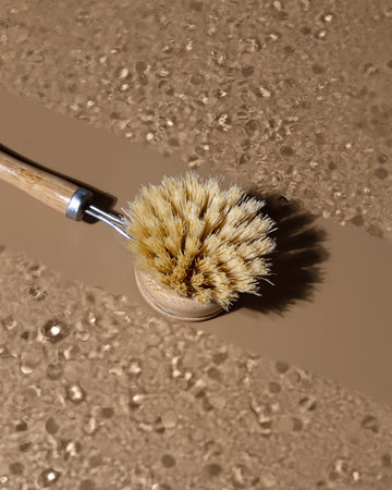Eco-friendly bamboo dishwashing brush with long wooden handle lying on glass with whater drops....