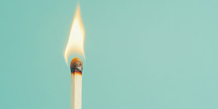 Closeup of a single burning matchstick with a bright flame set against a solid green background The image captures the vivid contrast and simplicityの素材