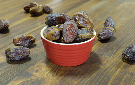 Dates in a red bowl on a wooden tableの写真素材