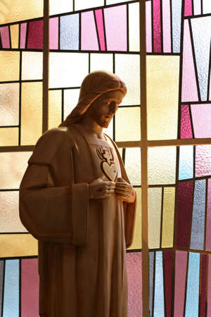 A jesus figure with punctured hands and heart in front of a modern stained glass windowのeditorial素材