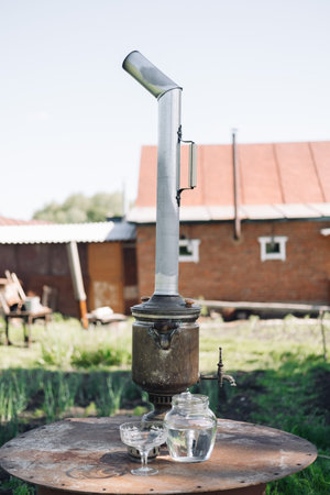 An antique samovar stands on a wooden table against the background of an old building.