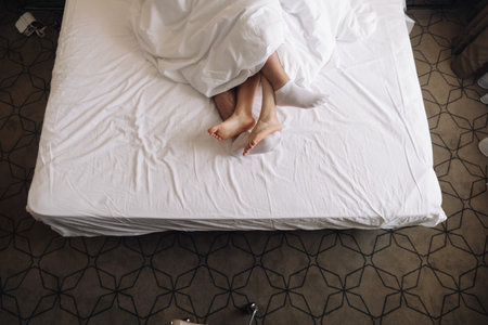 a woman and a man lie on a bed covered with a blanket in a white duvet cover and only their legs are...