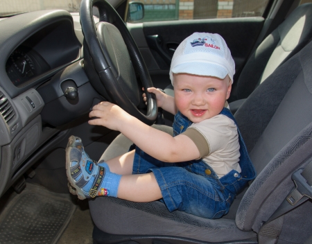 The little boy in a cap and a jeans suit at a car wheel の写真素材