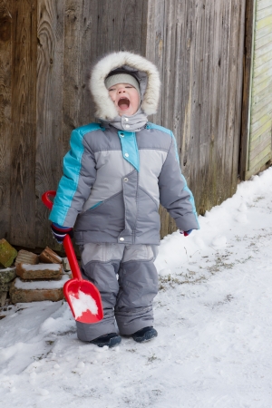 warmly dressed in overalls boy playing outdoors in snowy winterの写真素材