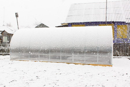 the greenhouse from plastic is located on the earth and covered by falling snowの写真素材