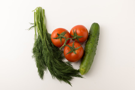 some small red tomatoes with a green branch and a cucumber with parsley and onions on a white backgroundの写真素材