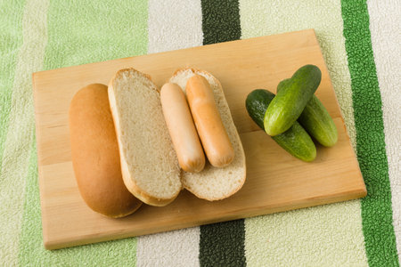 the sausage and bread with a cucumber lie on a wooden chopping boardの写真素材