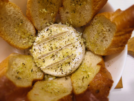 French camembert cheese baked in the oven with rosemary sprigs garlic cloves and bay leaves served with croutons on a wooden board on a dark wooden backgroundの写真素材