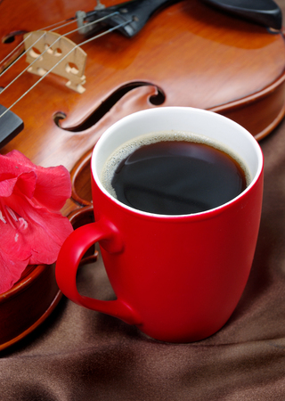 cup of coffee and a violin on a red silk backgroundの写真素材