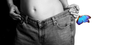 Slim girl in big jeans isolated on a white. A young woman shows a slimmed figure. Black and white. Weight loss concept. copy spaces.の写真素材