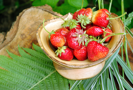 Ripe juicy strawberries in a wooden bowl. Handmade wooden vase from walnut.の写真素材