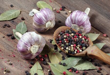 traditional spices for the kitchen. bay leaf, mixture of various peppers in a spoon and garlic on a wooden table.の写真素材