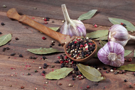 traditional spices for the kitchen. bay leaf, mixture of various peppers in a spoon and garlic on a wooden table.の写真素材