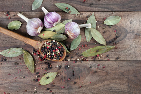 traditional spices for the kitchen. bay leaf, mixture of various peppers in a spoon and garlic on a wooden table.の写真素材
