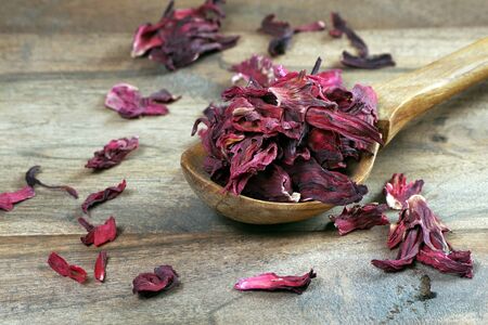 dry hibiscus in a wooden spoon. dried hibiscus petals on a wooden table. hibiscus tea. vitamin tea for cold and flu.の写真素材