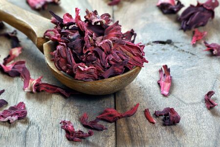 dry hibiscus in a wooden spoon. dried hibiscus petals on a wooden table. hibiscus tea. vitamin tea for cold and flu.の写真素材