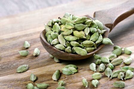 green cardamom pods in a wooden spoon on a wooden tableの写真素材