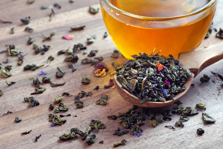 blended tea. green tea with dry flower petals. dry leaves of green tea in a wooden spoon and glass...
