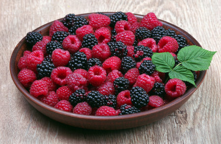 fresh ripe raspberries and blackberries in a bowl on a wooden table. summer healthy berries