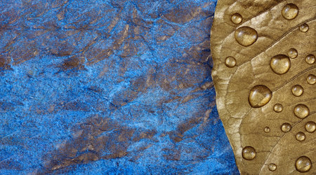 Golden leaf in drops of water on a blue watercolor background
