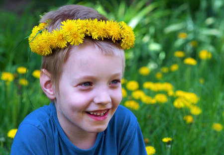 boy in a wreath of dandelions in a blooming meadow and bright red butterfly. summer concept. copy spaceの写真素材