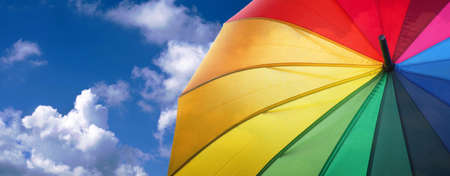 summer concept. good weather concept. colors of rainbow. colorful umbrella rainbow colors on blue sky background with cloudsの写真素材