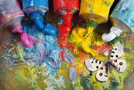 tubes with art oil paint on a palette and bright apollo butterfly. colorful art paints close-up