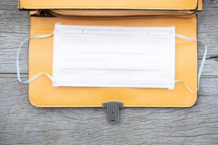 Yellow open leather bag and white mask on wood background. Space for objects or content for graphic...