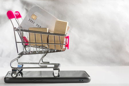 Paper box and credit card in shopping cart on black smartphone and white backdrop. online shopping...
