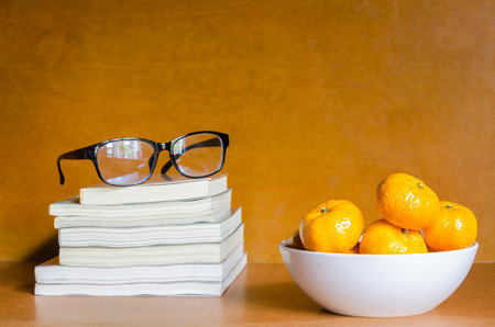 Group of oranges in white bowl and black glasses on books on wooden table and backgroundの写真素材