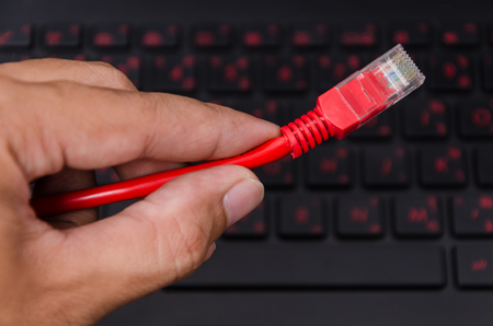 Red LAN Internet cable in man hand on black laptop computer with red back-light keyboard backgroundの写真素材