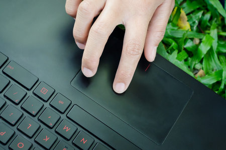 Woman finger touching on touchpad on black laptop computer above green grass