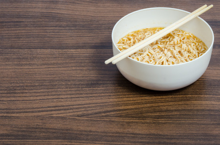 Hot instant noodle in white bowl and chopstick above wooden table with copy spaceの写真素材