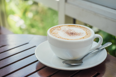 Hot cappuccino coffee above wooden table with morning sunlightの写真素材