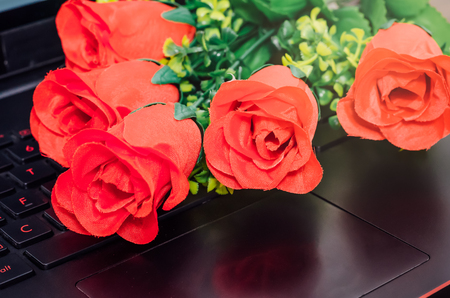 Red artificial plastic roses above black laptop computerの写真素材