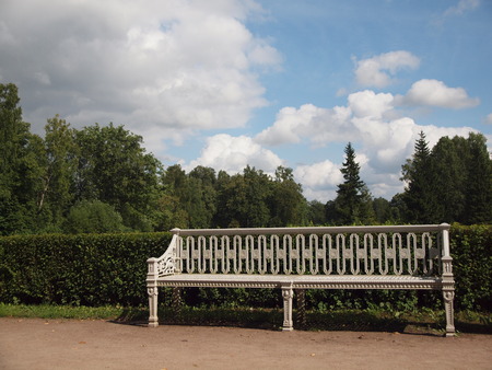 vintage white bench in the Park on the background of trimmed bushes, trees and cloudy skyの写真素材