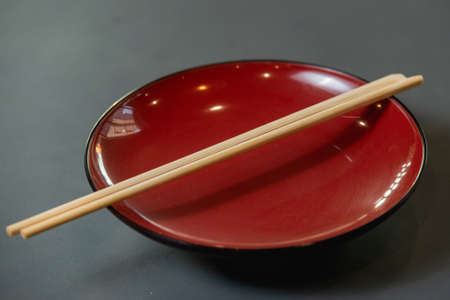 Empty red dish with chopsticks on grey background.の写真素材