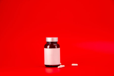 A pill bottle containing medication with pills visible on the side, set against a red backgroundの写真素材