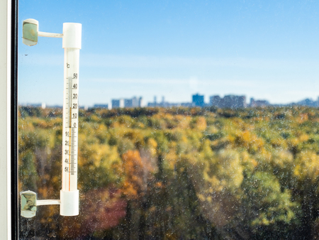 autumn background - sunny october day and view of blurry urban park through window glass (focus on thermometer)の写真素材