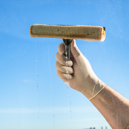 male hand wipes a window glass with blue sky on backgroundの写真素材