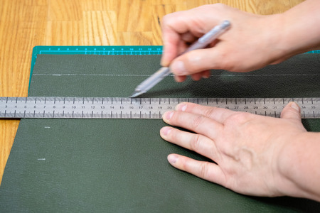 workshop of making textile and leather travel bag - craftsman draws a sketch on green leather using rullerの写真素材
