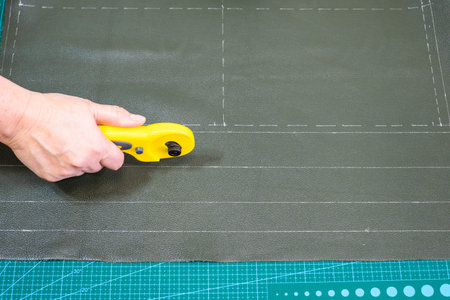 workshop of making textile and leather travel bag - craftsman cuts green leather using Rotary Cutter