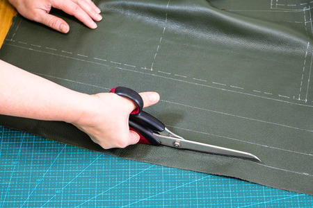 workshop of making textile and leather travel bag - craftsman cuts green leather using scissorsの写真素材