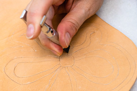 workshop of making the carved leather bag - craftsman carves flower on surface of rough vegetable...