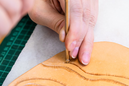 workshop of making the carved leather bag - craftsman stamps the relief on surface of rough vegetable tanned leather with Stamping tool close upの写真素材
