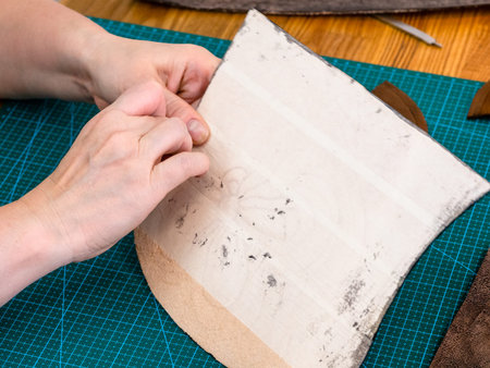 workshop of making the carved leather bag - craftsman removes the protective fabric from the back...