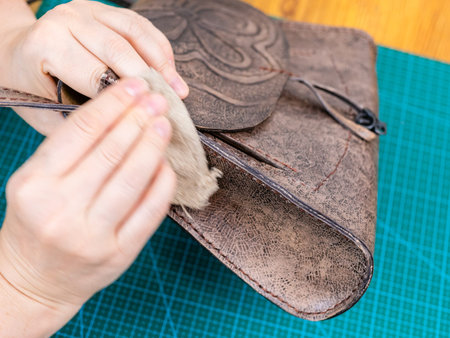 workshop of making the carved leather bag - craftsman polishes the handbag with wax