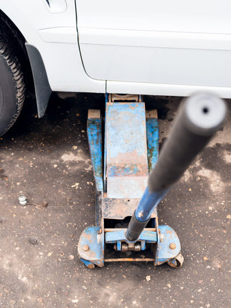 hydraulic jack lifts a car outdoors for seasonal replacement of tiresの写真素材