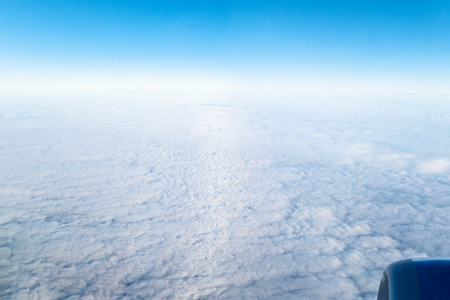 view of horizon between blue sky and cloudy surface through aircraft porthole during flightの写真素材